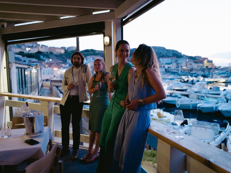 Invités debout sur la terrasse, verre à la main, face au port